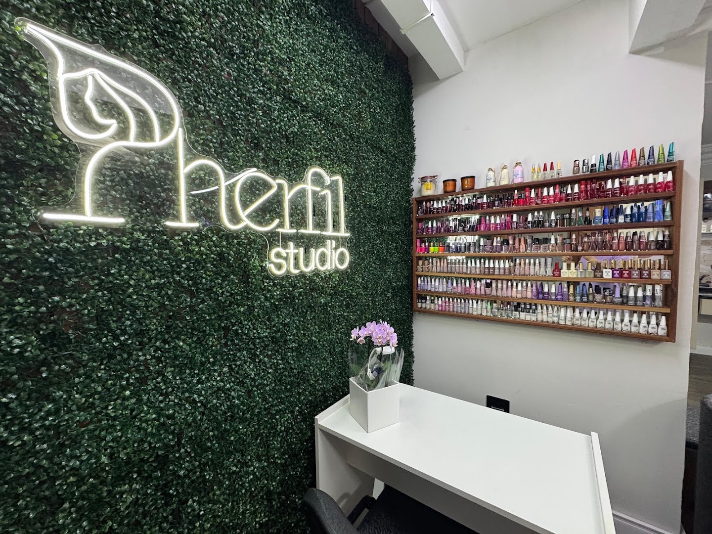 Parede com o logo iluminado do Pherfil Studio e prateleira de esmaltes